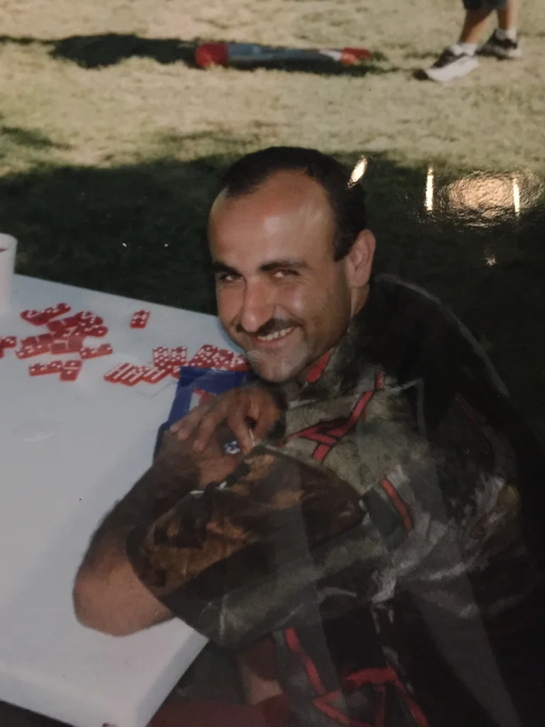 Danny’s uncle smiling while seated at an outdoor table with dominoes.