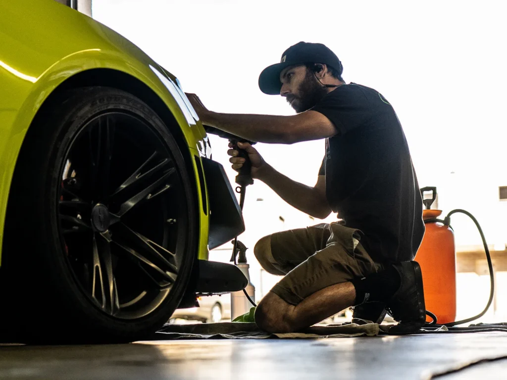 Installer fitting paint protection film around a green Chevrolet Camaro’s front bumper.