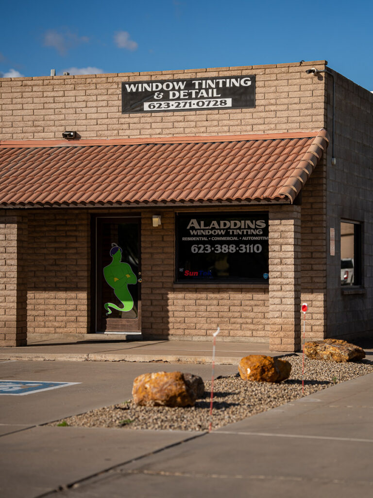 Aladdins Window Tinting storefront with dark tinted windows, brick walls, and a red tile awning.