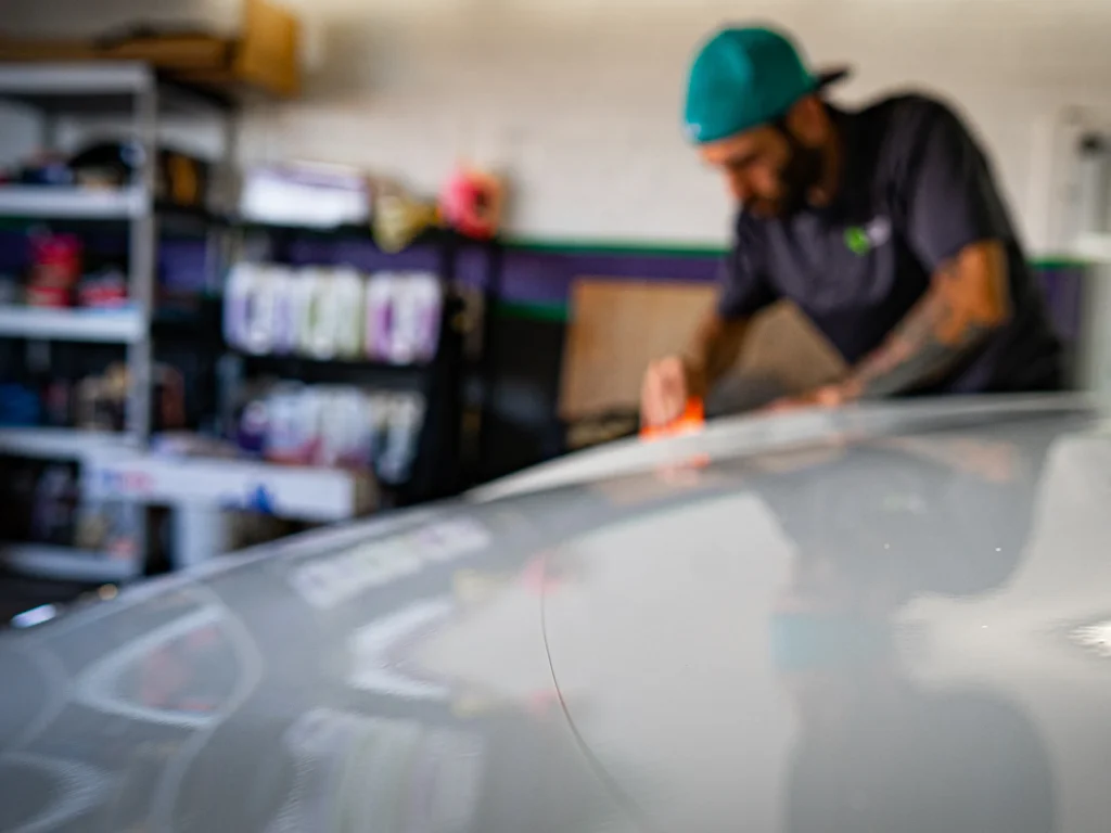 Installer smoothing paint protection film across a vehicle’s hood with an orange squeegee.