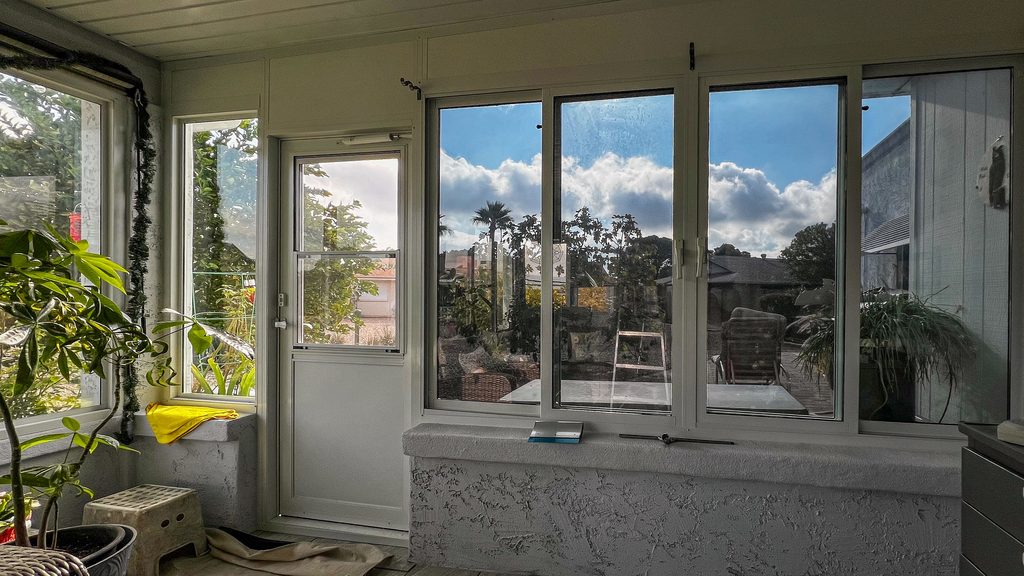 Sunroom with large windows overlooking a backyard, with potted plants and sunlight filtering through the glass.