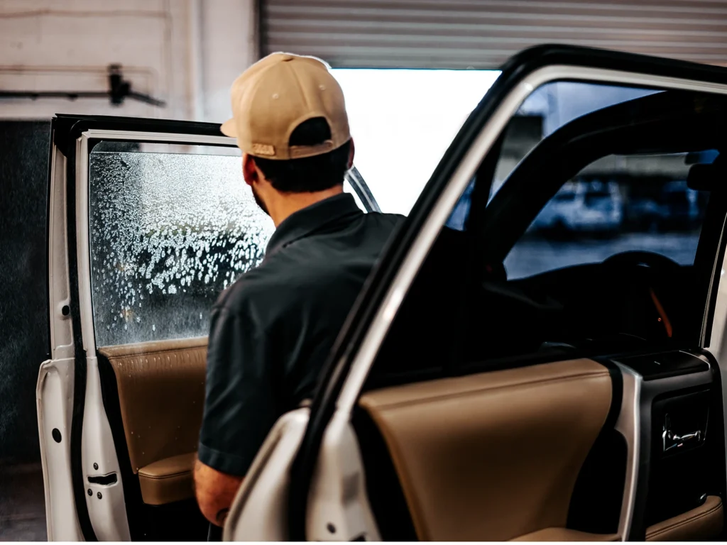 Installer applying SunTek Carbon window tint to a white vehicle’s side window at Aladdins Window Tinting.