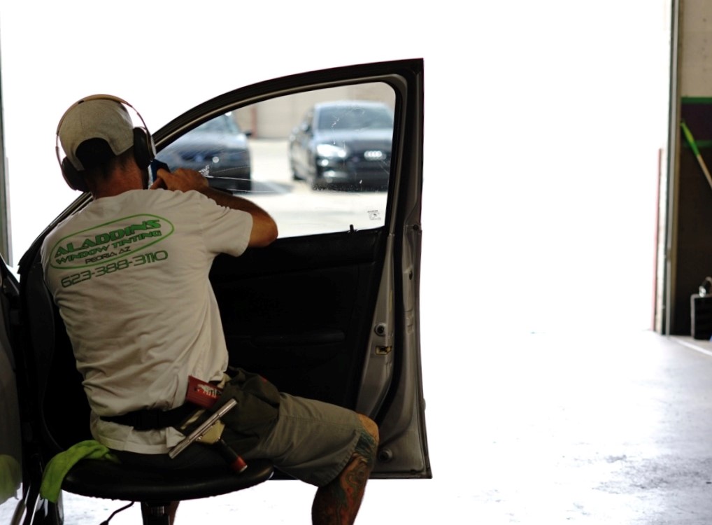 Aladdins Window Tinting installer applying window film to a vehicle’s front side window inside the shop.