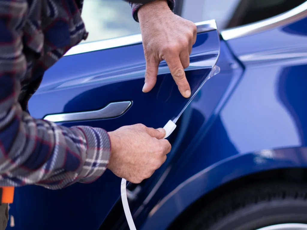 Installer applying clear protective film along a blue Tesla’s door edge.