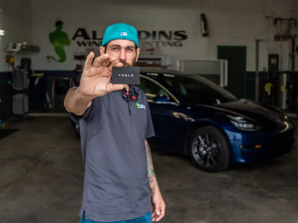 Technician holding a Tesla key card in front of a blue Tesla at Aladdins Window Tinting.