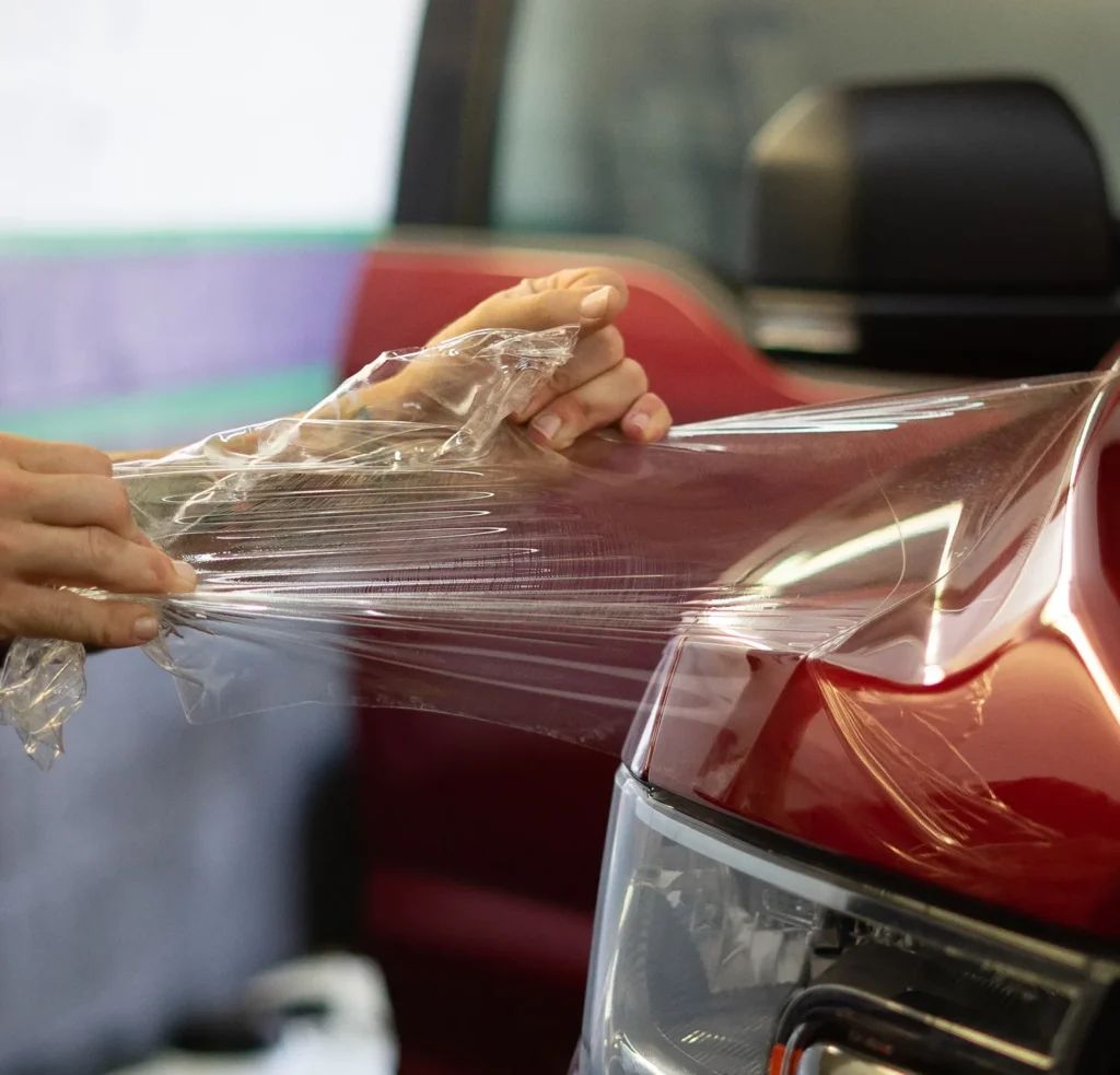 Installer removing clear paint protection film from a red truck’s hood.