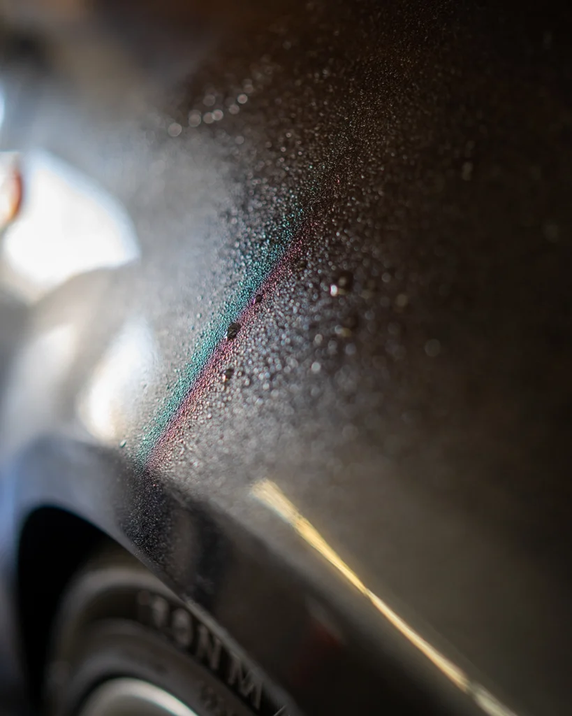 Close-up of water droplets on a dark vehicle’s body panel during surface preparation.