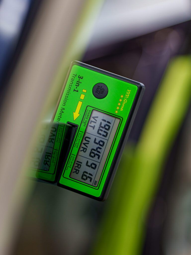 Digital window tint meter measuring visible light transmission, ultraviolet rejection, and infrared rejection through glass.